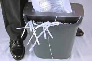 Man's Feet Standing Next to Shredder with Document In Process of Shredding